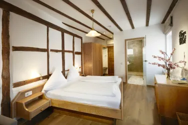 Ein gemütliches Zimmer mit einem Doppelbett und Holzdecke. Die Wände sind teilweise mit Fachwerk gestaltet und es gibt moderne Möbel.