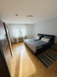 Ein gemütliches Schlafzimmer mit einem Doppelbett und zwei Fenstern. Der Boden ist aus Holz, und ein kleiner Teppich liegt neben dem Bett.