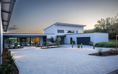 Ein modernes Haus mit klaren Linien und einem großzügigen Außenbereich. Die Umgebung ist grün und gut gepflegt.