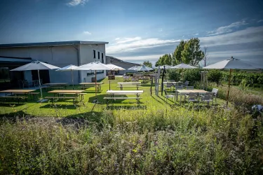 Ein schöner Außenbereich mit Tischen und Sonnenschirmen. Die Umgebung ist grün und lädt zum Verweilen ein.