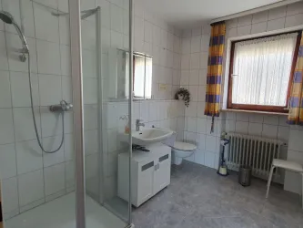 Ein modernes Badezimmer mit Dusche, Waschbecken und toilet. Helle Fliesen und Fenster sorgen für eine freundliche Atmosphäre.