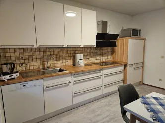 Eine moderne Küche mit weißen Schränken und Holzoberflächen. Die Ausstattung umfasst Spüle, Kaffeemaschine und Kühlschrank.