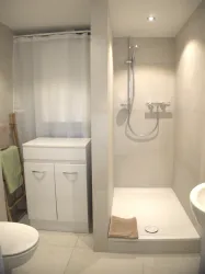 Ein modernes Badezimmer mit einer Dusche und hellen Fliesen. Es gibt einen weißen Schrank und eine schlichte, komfortable Gestaltung.