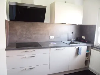 Moderne Küche mit schwarzem Kochfeld und Edelstahlarmatur. Die Wände sind in neutralen Farben gehalten, und es gibt praktische Ablageflächen.