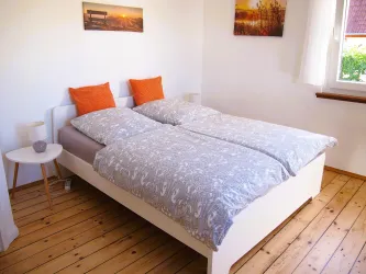 Ein gemütliches Schlafzimmer mit einem großen Bett und orangefarbenen Kissen. Der Boden ist aus Holz und es gibt einige Bilder an der Wand.
