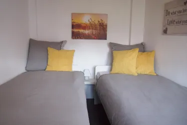 Ein gemütliches Zimmer mit zwei Betten und hellen Kissen. An der Wand hängt ein Bild einer Landschaft.