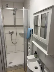 Eine moderne Dusche mit klaren Fliesen und einem Handtuch. Rechts befindet sich ein kleiner Waschplatz mit einem Spiegelschrank.