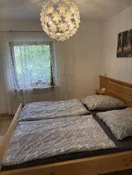 Ein gemütliches Schlafzimmer mit einem Doppelbett und einem modernen Kronleuchter. Das Fenster bietet einen Blick auf das grüne Umfeld.