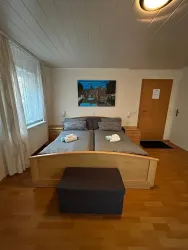 Ein gemütliches Apartment mit Doppelbett und einem kleinen Hocker. An der Wand hängt ein Bild, das eine idyllische Landschaft darstellt.