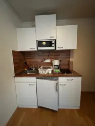 Eine kleine moderne Küche mit weißen Schränken. Sie ist ausgestattet mit einem Spülbecken, einem Kühlschrank und einer Mikrowelle.