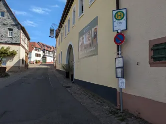 Eine ruhige Straße mit historischen Häusern und einem Buswartehäuschen. Die Atmosphäre ist entspannt und einladend.