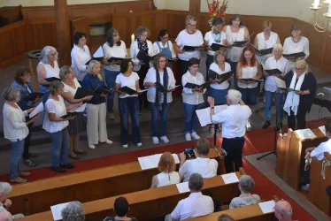 Ein gemischter Chor singt in einer Kirche. Der Chorleiter steht vorne und leitet die Sänger.