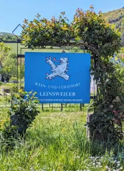 Ein Schild zeigt den Ort Leinsweiler als Wein- und Ferienort an. Umgeben von üppigem Grün und Weinbergen ist es ein malerischer Anziehungspunkt.