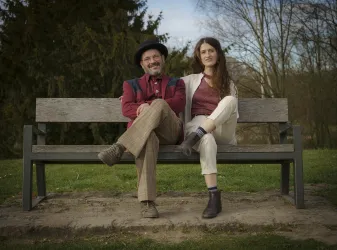 Ein Mann und eine Frau sitzen entspannt auf einer Bank im Freien. Sie lächeln und genießen die Natur um sich herum.
