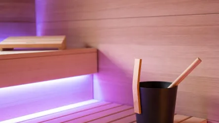 Eine moderne Sauna mit Holzregalen und sanfter Beleuchtung. Ein Eimer und ein Schöpflöffel stehen bereit für den Saunagang.