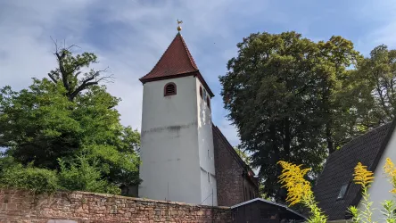 Ein historischer Kirchturm mit rotem Dach, umgeben von hohen Bäumen. Die Szene strahlt eine ruhige und ländliche Atmosphäre aus.
