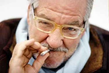 Ein Musiker singt und spielt Gitarre, während eine Cellistin neben ihm spielt. Hintergrundlich sind bunte Lichter zu sehen, die eine lebendige Atmosphäre schaffen.