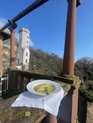 Ein Teller mit Suppe steht auf einem Tisch im Freien. Im Hintergrund ist ein historischer Turm und ein blauer Himmel zu sehen.