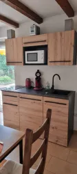 Eine moderne Küche mit Holzschränken und einer schwarzen Arbeitsfläche. Sie enthält eine Mikrowelle, eine Kaffeemaschine und eine elegante Spüle.