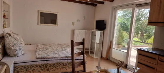 Ein gemütliches Zimmer mit einem Bett, einem Tisch und einem Stuhl. Große Fenster bieten Blick auf einen grünen Garten.