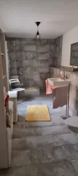 Ein modernes Badezimmer mit grauen Fliesen und einem Waschbecken. Es gibt einen beigen Teppich und eine Dusche in der Ecke.
