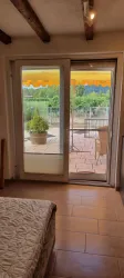 Ein heller Raum mit einer offenen Tür zum Außenbereich. Der Blick zeigt eine Terrasse mit Pflanzen und einem gelben Sonnenschirm.