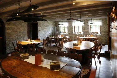 Ein rustikales Restaurant mit Holzstühlen und großen Tischen. Die Wände sind aus Stein, und es gibt Fenster mit natürlichem Licht.