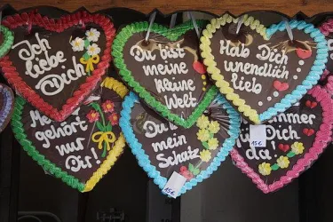 Bunte Lebkuchenherzen mit liebevollen Sprüchen hängen an einer Wand. Die Herzen zeigen romantische Botschaften und sind mit essbarem Zuckerguss verziert.