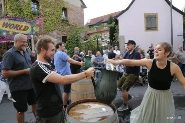 Ein fröhliches Fest mit Menschen, die an einem Wettbewerb teilnehmen. Sie stehen um Fässer und interagieren miteinander, während eine Menschenmenge zusieht.