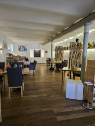 Ein modernes Restaurant mit Holzböden und eleganter Ausstattung. Es gibt Tische mit Stühlen und eine gemütliche Atmosphäre.