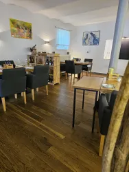 Ein modernes Restaurant mit Holzböden und eleganten Tischen. Die Wände sind hell gestrichen und mit kunstvollen Bildern dekoriert.