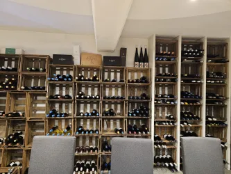 Ein Weinlager mit Holzregalen, die viele Flaschen Wein enthalten. Im Vordergrund sind mehrere Stühle sichtbar.