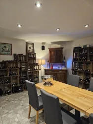 Ein gemütlicher Weinkeller mit Regalen voller Weinflaschen. In der Mitte steht ein Holztablett mit einem silbernen Kübel und einem Tisch mit modernen Stühlen.