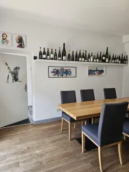Ein moderner Essbereich mit einem Holzstuhl und einem langen Tisch. An der Wand stehen viele Weinflaschen, während einige Bilder den Raum dekorieren.