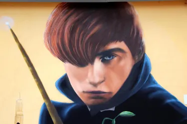Ein großes Wandgemälde eines jungen Mannes mit rotem Haar. Er trägt einen blauen Mantel und hält einen Stab in der Hand.