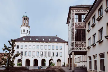 Ein historisches Rathaus mit einem markanten Turm und modernen Gebäuden daneben. Der Platz ist ruhig und einladend.