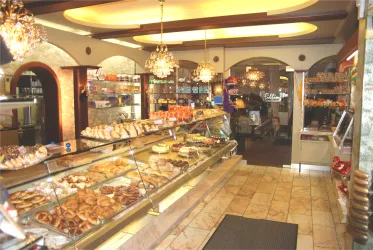 Eine gemütliche Bäckerei mit einer Vielzahl von Gebäck und süßen Leckereien in der Auslage. Die Inneneinrichtung ist hell und einladend, mit glitzernden Kronleuchtern.