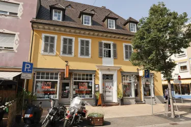 Ein Farbiges Gebäude mit gelber Fassade und mehreren Fenstern. Davor stehen Motorräder und ein paar Bäume.