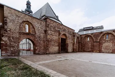 Eine historische Ruine mit hohen Mauern und einem Tor. Der Platz davor ist leer und von Gras umgeben.