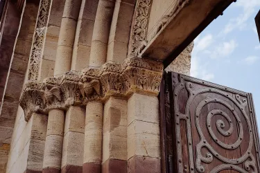 Ein historisches Gebäude mit kunstvoll verzierten Säulen und einem großen Holztor. Der Himmel ist leicht bewölkt und verleiht der Szene eine ruhige Atmosphäre.