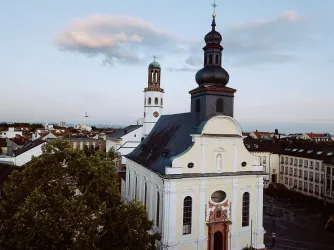 Eine schöne Kirche mit einer markanten Kuppel und einem hohen Turm. Im Hintergrund sind einige Gebäude und ein klarer Himmel zu sehen.