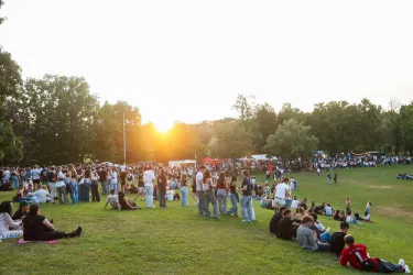 Eine große Menschenmenge versammelt sich im Park bei Sonnenuntergang. Viele sitzen auf dem Gras und genießen die Atmosphäre.