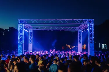 Eine Menschenmenge bei Nacht auf einem Musikfestival. Die Szenerie wird von bunten Lichtern und einer festlichen Atmosphäre geprägt.