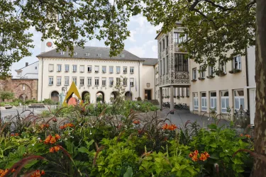 Ein schöner Innenhof mit bunten Blumen und modernen Gebäuden. Im Hintergrund steht eine große, historische Fassade.