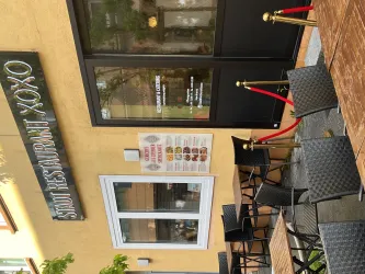 Das Bild zeigt ein Restaurant mit dem Namen "XOXO". Vor dem Restaurant stehen Tische und Stühle sowie ein roter Teppich.