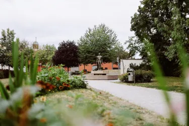 Ein schöner Park mit einer Statue in der Mitte. Umgeben von grünen Bäumen und bunten Blumen.