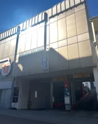 Ein modernes Parkhaus mit glänzender Fassade. Ein Parkplatzzeichen ist gut sichtbar neben dem Eingang.