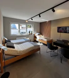 Ein modernes Schlafzimmer mit zwei Einzelbetten und einem Schreibtisch. Große Fenster lassen viel Tageslicht herein.