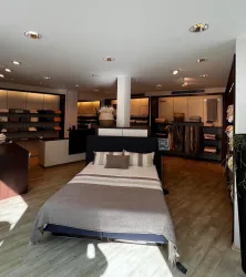 Ein modernes Schlafzimmer mit einem Bett und verschiedenen Bettwaren. Der Raum hat helles Licht und eine angenehme Atmosphäre.