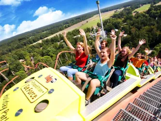 Im Zentrum des Bildes ist eine Achterbahn mit Gästen des Holiday-Parks zu sehen die ihre Arme heben und schreien.